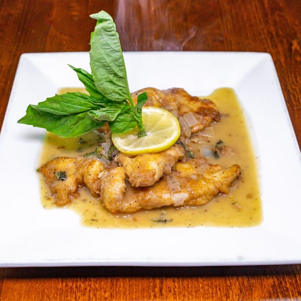 Steaming chicken piccata with lemon, basil, and a creamy sauce on a white plate.