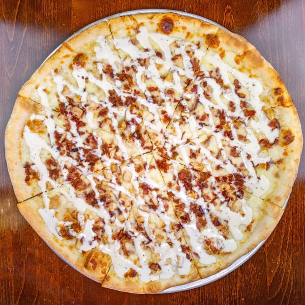 Zio's Pizzeria's chicken bacon ranch pizza, sliced and drizzled with white sauce on a wooden table.