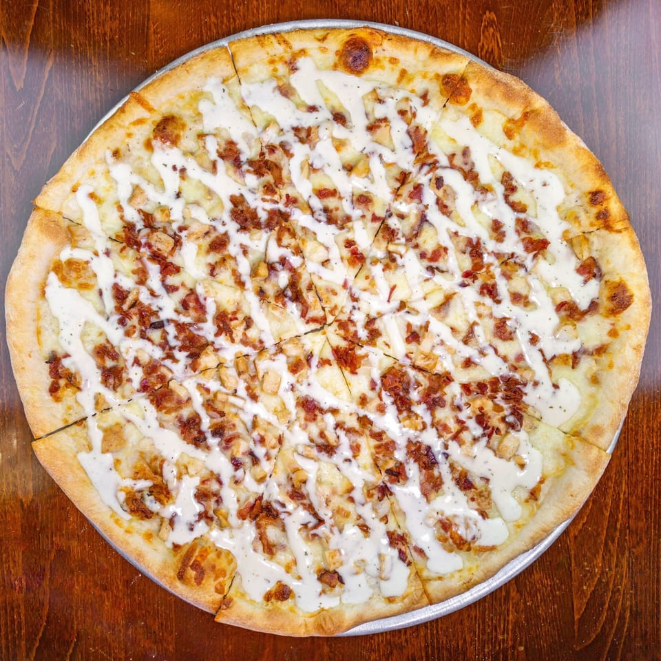 Zio's Pizzeria's bacon ranch pizza, drizzled with white sauce and cut into slices.