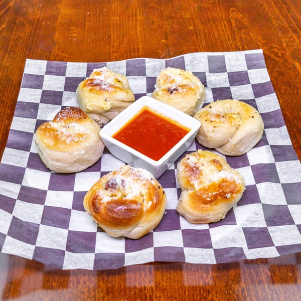 Six Zio's Pizzeria garlic knots with parmesan cheese and a side of marinara sauce.