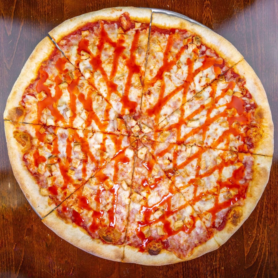 A Zio's Pizzeria buffalo chicken pizza, cut into slices, with a spicy red sauce drizzle.