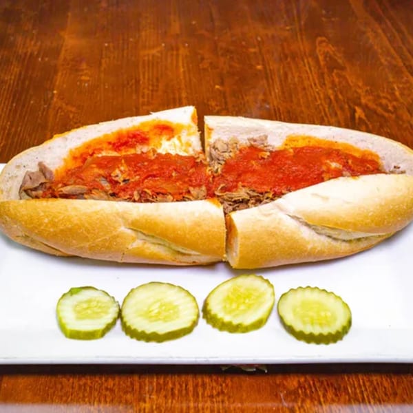 A Zio's Pizzeria Italian beef sandwich, cut in half, with four pickle slices on a white plate.