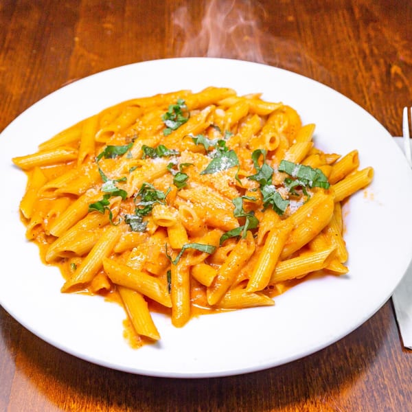 Steaming penne pasta with creamy red sauce, grated cheese, and fresh basil on a white plate.