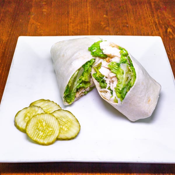 Chicken Caesar wrap, cut in half, with a side of pickle slices on a white plate.