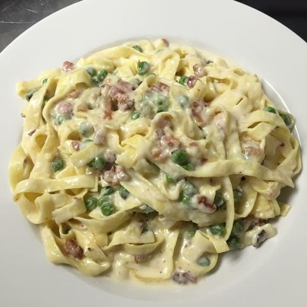 Creamy fettuccine pasta with green peas and bacon bits on a white plate.